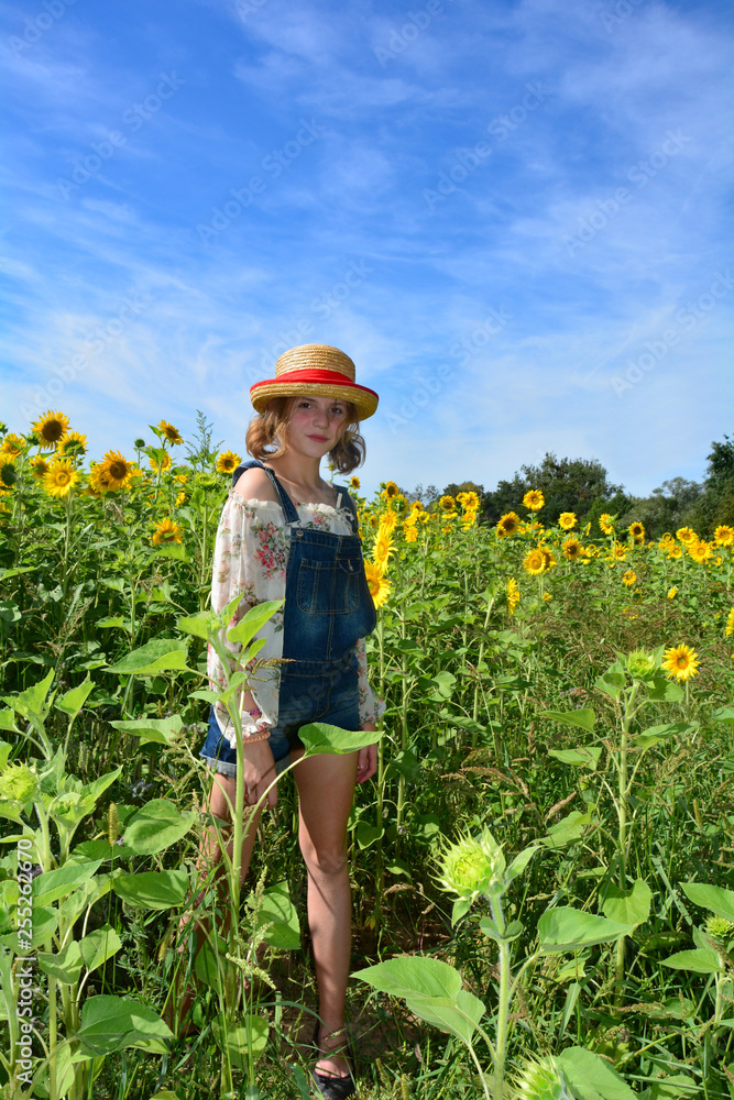 Mädchen  steht mit kurzer Jeans und Hut im Sonnenblumen Feld mit blauem Himmel