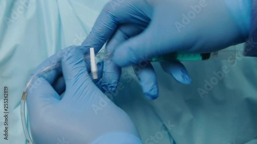 Gloved medical hands use syringe to insert blue liquid into tube or IV