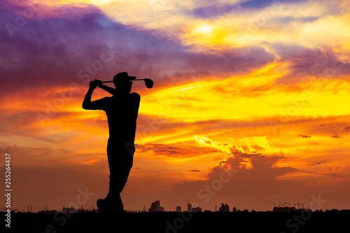Silhouette of golfer hit sweeping on sunset background. Golfer young man playing golf during beautiful sunrise sky with city.