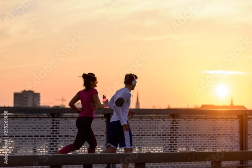 Young man and woman jogging together over bridge in the sunset