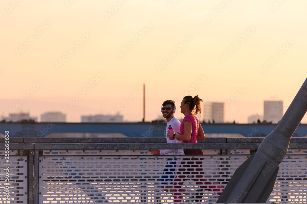 Young man and woman jogging together over bridge in the sunset Young man and woman jogging together over bridge in the sunset