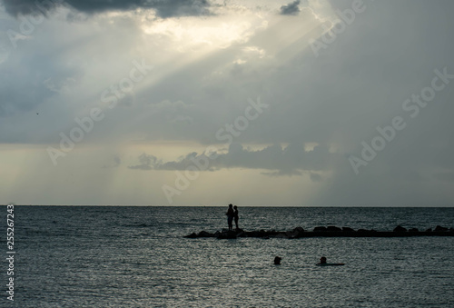 beach in Florida on the Gulf of Mexico with a cloudy sky with light shining through and rain in the distance. A lone fisherman stands on the jetty