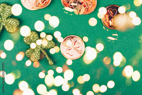 Glitter shamrocks and golden coins on green paper background. St Patricks day symbol. Irish National holiday concept. Bold festive bokeh