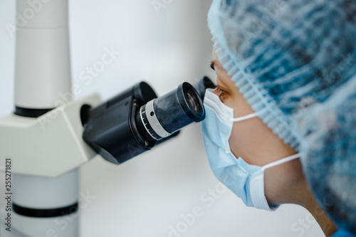 Researcher gaze into the eyepieces of a large laboratory microscope against a blurred background of a scientific laboratory