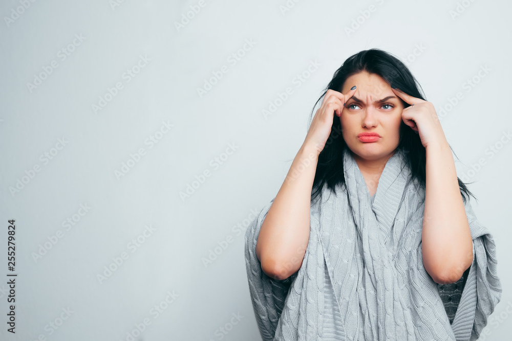 Upset girl in a gray robe indicates poor skin, age wrinkles, acne on a white and gray studio background. A woman is looking for flaws and age changes. Upset girl in a gray robe indicates poor skin, age wrinkles, acne on a white and gray studio background. A woman is looking for flaws and age changes.