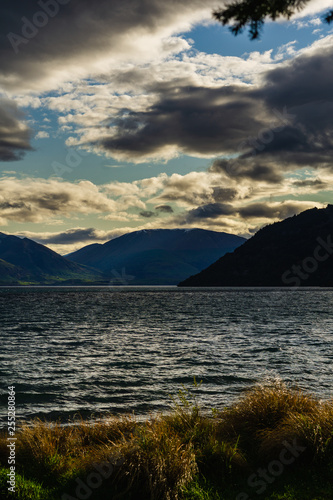 peaceful landscape during sunset with dramatic sky above the lake and mountain range, grass in the foreground