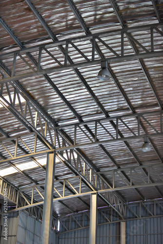 An interior space of a factory shop showing a scaffolding metal roof sheet with a framework of metal truss with sunlight goes through. © athichoke.pim