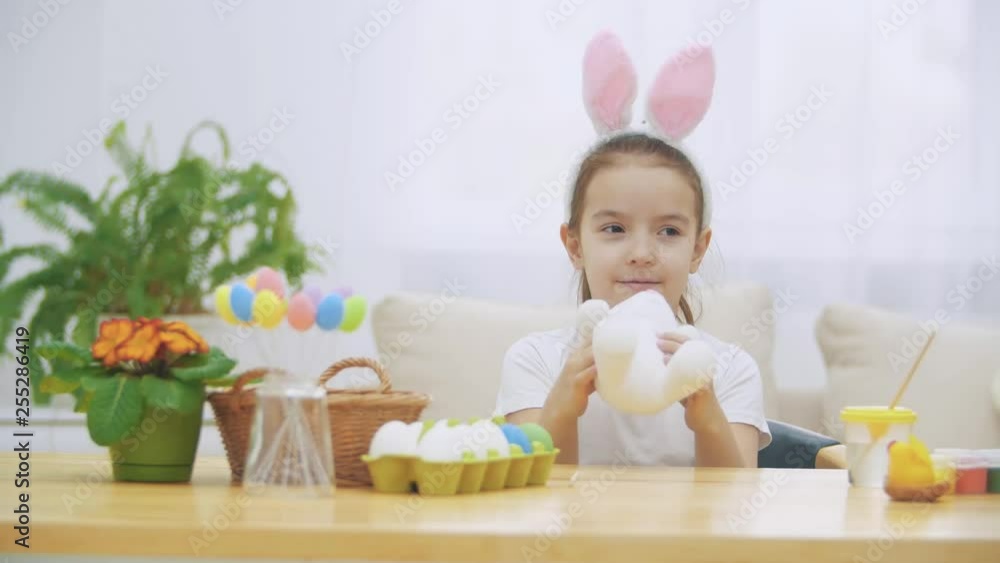 Little cute and adorable girl is smiling and playing with bunny's ears. Concept Easter holiday. Little cute and adorable girl is smiling and playing with bunny's ears. Concept Easter holiday.