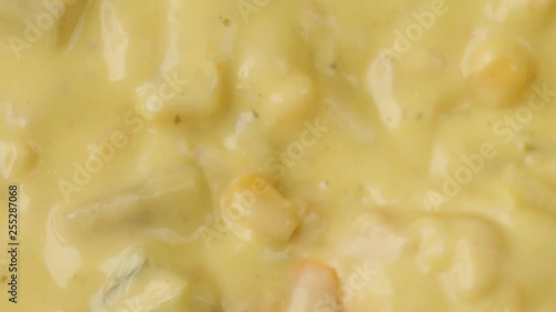 Very close video of stirring and taking a spoonful of chicken corn chowder illuminated with natural lighting.