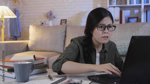 Worried sad student female searching information in a laptop online at home at night. young girl frowning typing on keyboard to solve the computer cased on notebook. unhappy lady in annoying face.