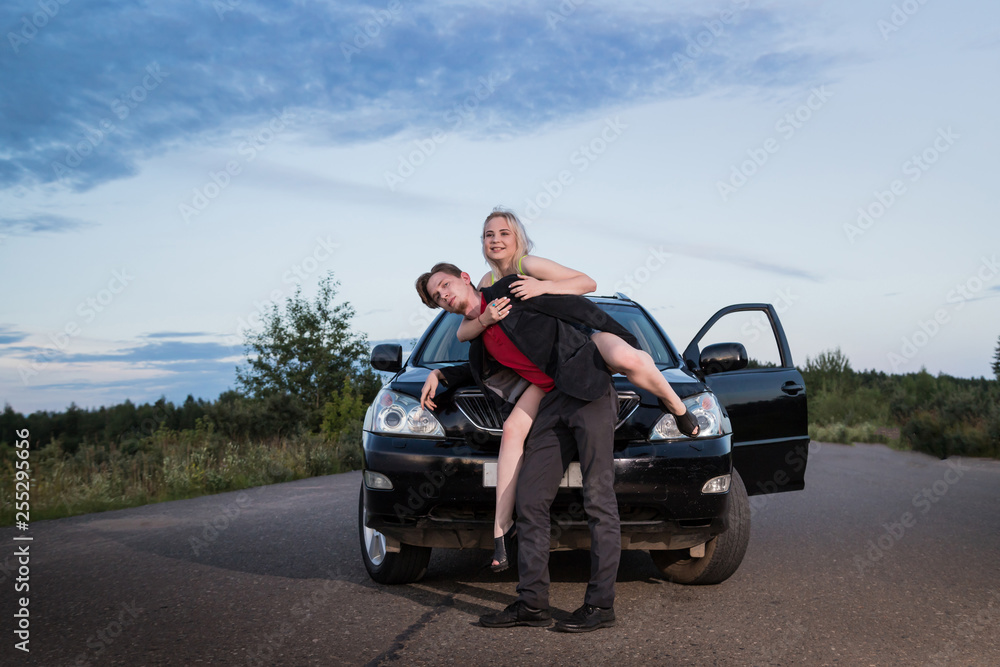 Guy carrying the girl on the road near the car in a summer evening Guy carrying the girl on the road near the car in a summer evening