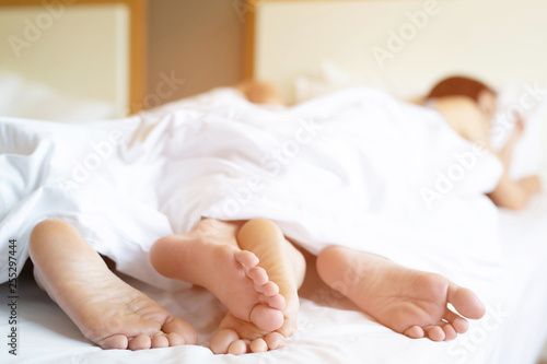 close up legs feet of two Lovers couple sleeping side by side embracing under blanket white sheets in bed at home on holiday concept having sexual romantic moments. Leave copy space to write text.