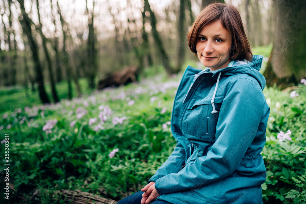 Toned photo of happy hiking middle-aged woman in blue jacket sitting and resting in evening spring forest Toned photo of happy hiking middle-aged woman in blue jacket sitting and resting in evening spring forest