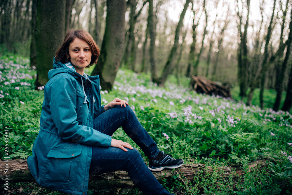 Toned photo of happy hiking middle-aged woman in blue jacket sitting and resting in evening spring forest Toned photo of happy hiking middle-aged woman in blue jacket sitting and resting in evening spring forest