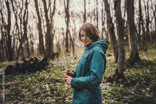 Toned photo of happy hiking middle-aged woman in blue jacket standing and resting in evening spring forest