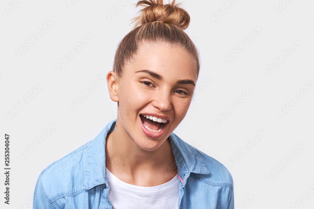 Close up image of charming positive young woman dressed in casual outfit with pleasant broadly smile, looking to the camera and posing over white studio wall. People emotions concept Close up image of charming positive young woman dressed in casual outfit with pleasant broadly smile, looking to the camera and posing over white studio wall. People emotions concept