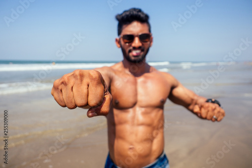 Topless athletic  muscular and healthy black man warm up instructor on the beach.indian male fashion model with denim shorts jeans and perfect body.healthy food and active beach vacation