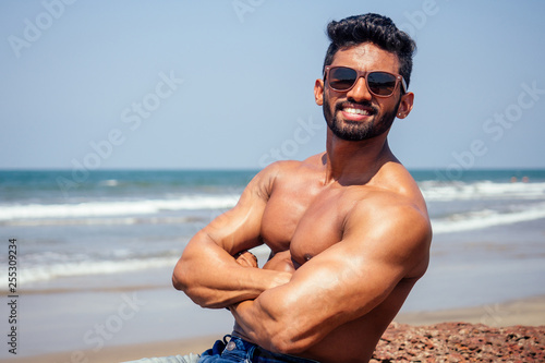 portrait of happy young african man on the beach.Handsome and confident Masculine hard fitness model male body bodybuilder with six pack.India trainer with perfect abs, shoulders,biceps, triceps,chest