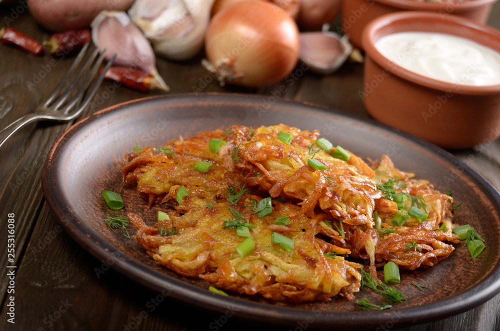 Fresh homemade tasty potato pancakes in clay dish with vegetables on wooden table Fresh homemade tasty potato pancakes in clay dish with vegetables on wooden table