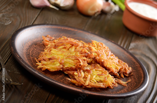 Fresh homemade tasty potato pancakes in clay dish on wooden table