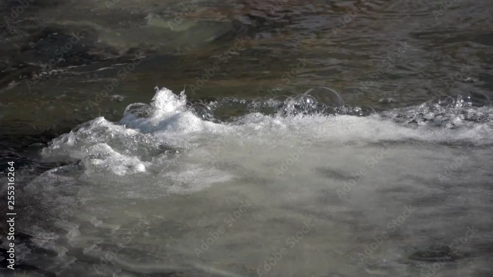 Water rushing in an icy frozen river making foam bubbles on the surface Water rushing in an icy frozen river making foam bubbles on the surface