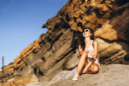 Pretty long hair brunette tourist girl relaxing on the stones near sea.