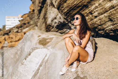 Pretty long hair brunette tourist girl relaxing on the stones near sea.