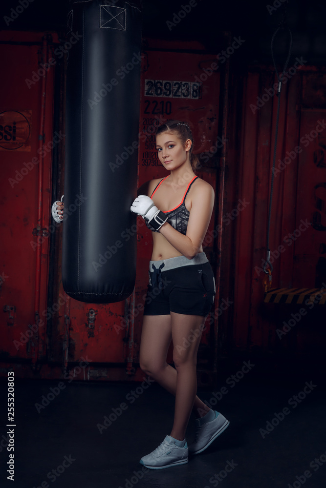 Fitness class. Young beautiful sports woman wearing gloves posing on the background of boxing gym