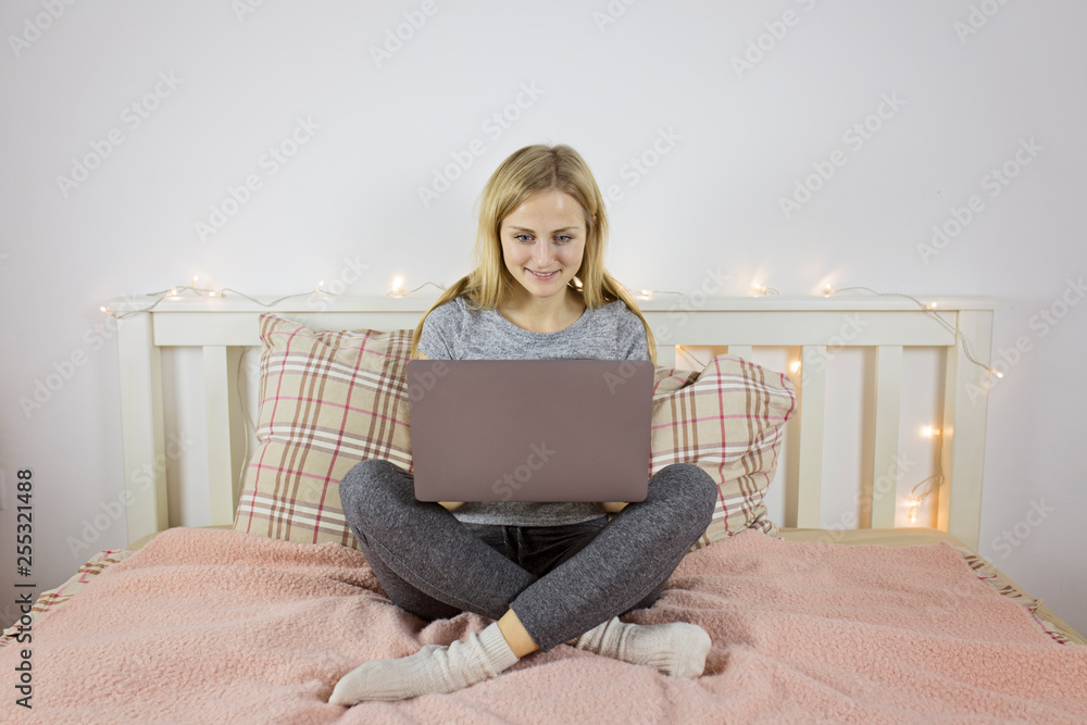 Attractive girl working behind a laptop sitting on the bed