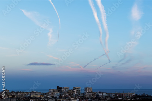 Many airplane contrails in a clear sky over the city. Jets of airplane in the blue sky.
