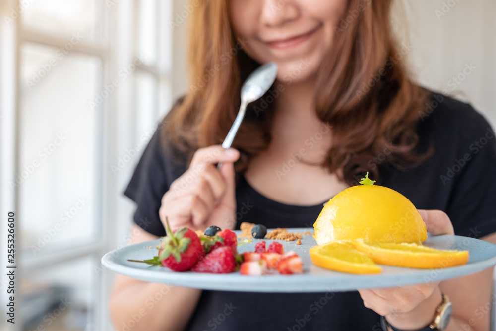 A beautiful asian woman holding a plate of orange cake with mixed fruit and a spoon in cafe A beautiful asian woman holding a plate of orange cake with mixed fruit and a spoon in cafe