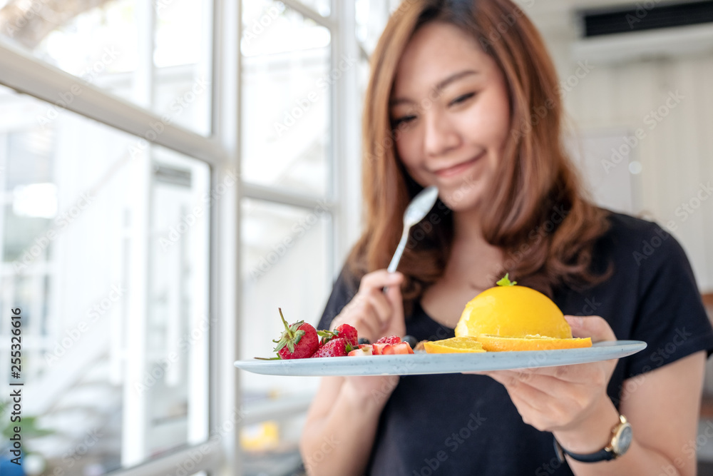 A beautiful asian woman holding a plate of orange cake with mixed fruit and a spoon in cafe A beautiful asian woman holding a plate of orange cake with mixed fruit and a spoon in cafe