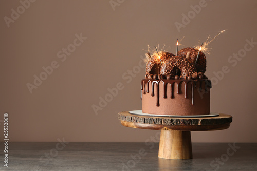 Fotografía Sweet chocolate cake with sparklers on table against color background