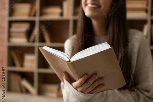 Beautiful young woman reading book in library, closeup photo