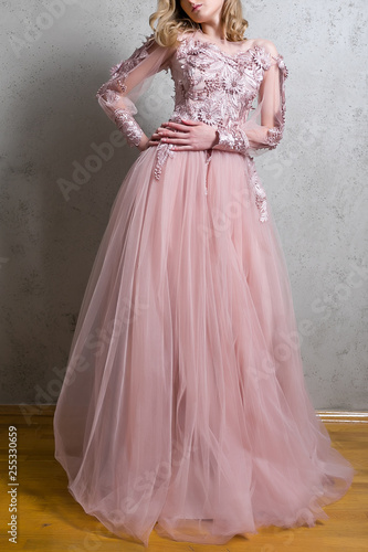 A girl in a long pink tulle dress with embroidery in the shape of flowers isolated on a gray background.