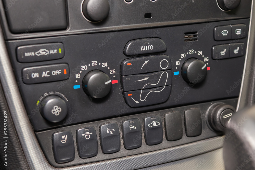 The central control console on the panel inside the car close-up with climate control and audio system and a hole for the CD and emergency button in gray and black. The central control console on the panel inside the car close-up with climate control and audio system and a hole for the CD and emergency button in gray and black.
