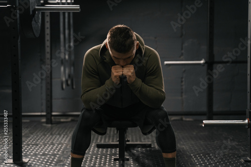 Strong sporty man sitting on gym bench suffering breakdown to overcome. photo