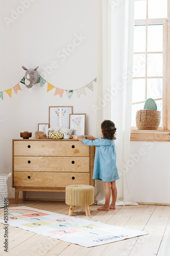 Little girl wearing light blue dress playing in children room scandinavian style.