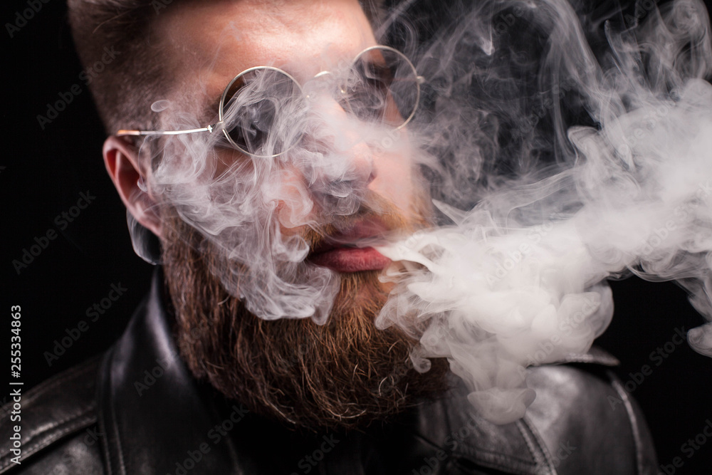 Close up portrait of bearded young man with sunglasses exhaling cigarette smoke over background Close up portrait of bearded young man with sunglasses exhaling cigarette smoke over background