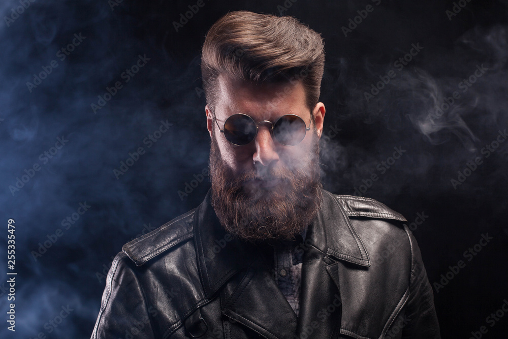 Rich handsome bearded man with sunglasses and leather jacket over black background