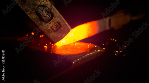 Photo MACRO: Small black particles flying away from hot red blade while getting forged
