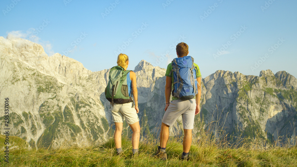 Unrecognizable carefree hiker couple observes the idyllic mountains on sunny day