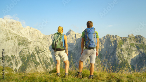 Unrecognizable carefree hiker couple observes the idyllic mountains on sunny day