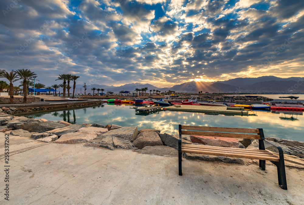Coastal landscape with a wooden bench on stone walking pier as foreground, Eilat, Israel