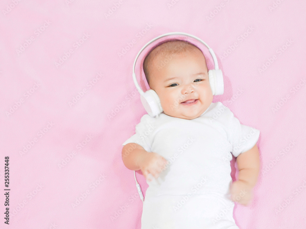 Asian baby girl wears white headphone and white shirt on pink background Asian baby girl wears white headphone and white shirt on pink background