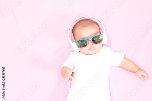 Asian baby girl wears white headphone and white shirt on pink background © StockerThings