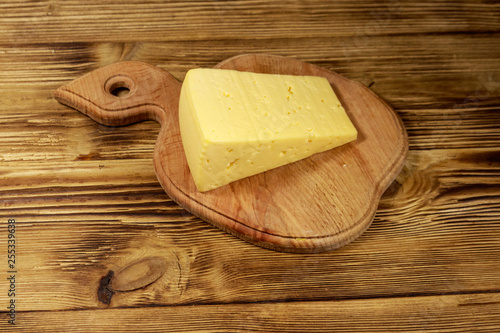 Piece of cheese on cutting board on wooden table