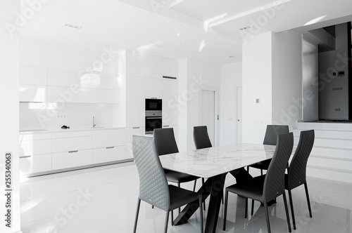 Luxurious modern dining room with white table, black chairs and white modern kitchen.  Minimalistic style.