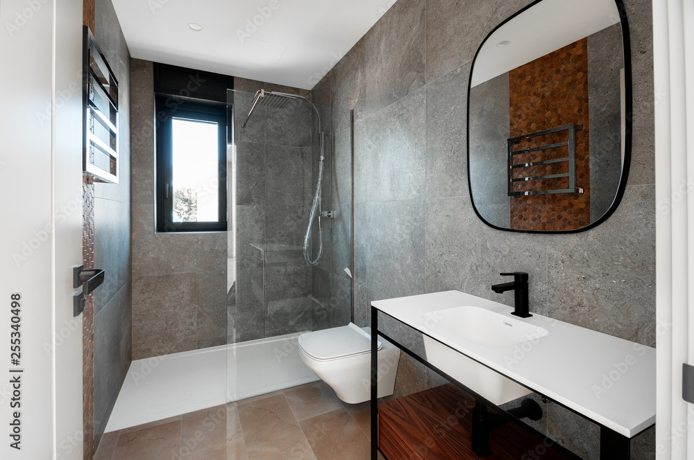 Modern bathroom with a glass bathtub and luxury washbasin. The walls and floor are covered with modern tiles.
