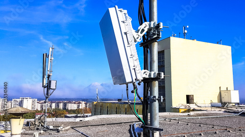 5G mobile telecommunication smart cellular radio network antennas on a mast on the roof broadcasting signal waves over the city on a clear sunny day with blue sky and clouds close up